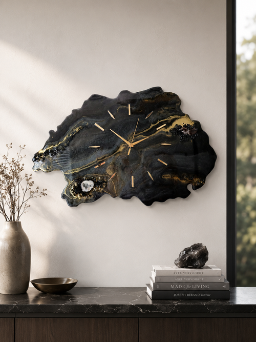 An organic-shaped black and gold agate wall clock with gold-tone hands, mounted on a light gray wall above a dark marble console table with decorative books and a vase.